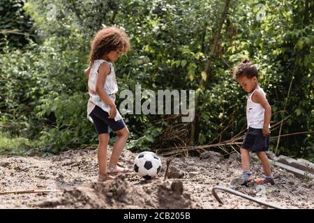 Focalizzazione selettiva dei bambini afro-americani indigenti che giocano a calcio strada sporca sulla strada urbana Foto Stock