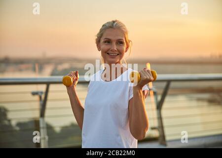 Donna sportiva con le braccia piegate che reggono pesi Foto Stock