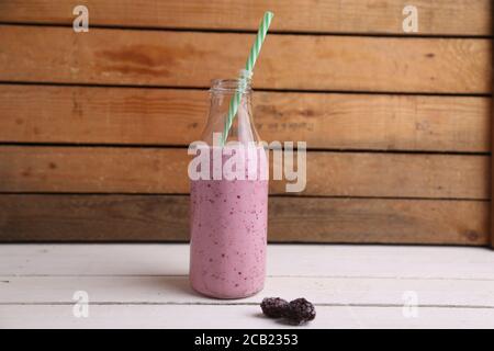 Frullato di frutti di bosco fresco in una bottiglia di vetro decorativo su un sfondo di legno Foto Stock