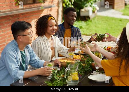 Gruppo multietnico di persone che condividono il cibo mentre si gusta la cena con gli amici e la famiglia all'aperto durante la festa estiva, spazio fotocopie Foto Stock