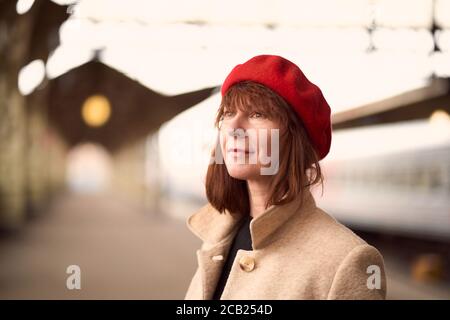 Primo piano ritratto di bella donna, sorridente e in attesa di treno sulla stazione ferroviaria. La ragazza viaggia leggero Foto Stock