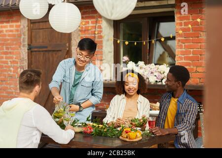 Gruppo multietnico di amici seduti a un tavolo di legno mentre si gusta la cena all'aperto durante la festa estiva, spazio fotocopie Foto Stock