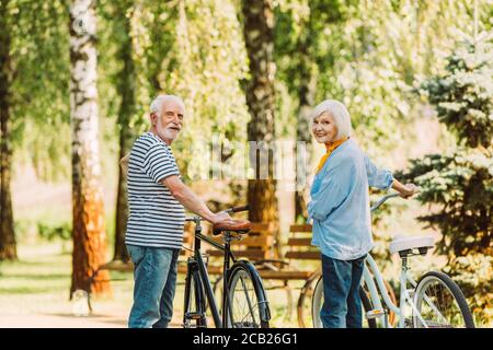 Coppia senior sorridente alla macchina fotografica mentre si sta in piedi vicino alle biciclette parcheggio Foto Stock