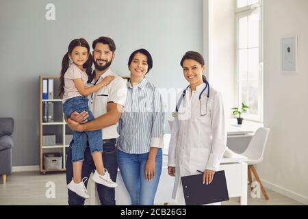 Famiglia alla consultazione di un medico presso la clinica. I genitori con il bambino e la donna terapeuta sorridono mentre si levano in piedi nell'ufficio dell'ospedale. Medico Foto Stock