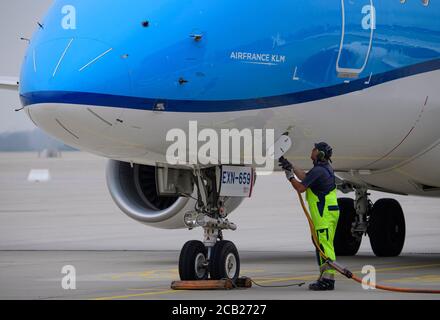 03 agosto 2020, Sassonia, Dresda: Un membro del personale di terra collega l'alimentazione all'aeromobile dopo l'atterraggio di un Embraer della compagnia aerea olandese KLM all'aeroporto internazionale di Dresda da Amsterdam-Schiphol. L'aeroporto di Dresda è stato nuovamente collegato al centro internazionale Amsterdam-Schiphol da lunedì dopo una pausa obbligatoria di oltre quattro mesi a causa della pandemia di Corona. KLM Royal Dutch Airlines sta inizialmente volando la rotta cinque volte alla settimana, con sei collegamenti settimanali programmati da settembre in poi e collegamenti giornalieri da ottobre in poi, Mitteldeutsche Flughafen AG Foto Stock