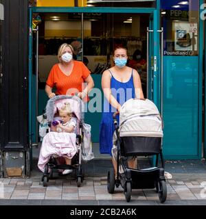 I clienti che indossano maschere facciali lasciano Poundland a Belfast poiché i rivestimenti facciali sono ora obbligatori per gli acquirenti nell'Irlanda del Nord. Foto Stock