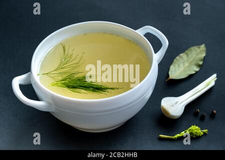 Brodo fatto in casa di ossa di carne in un tureen, verdure e condimenti, su sfondo nero. Alimentazione sana concept.Paleo dieta. Messa a fuoco selettiva.primo piano. Foto Stock