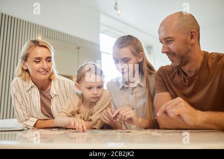 Ritratto a basso angolo dai toni caldi della famiglia moderna con due bambini che risolvono il puzzle insieme mentre si gode il tempo in casa, copia spazio Foto Stock