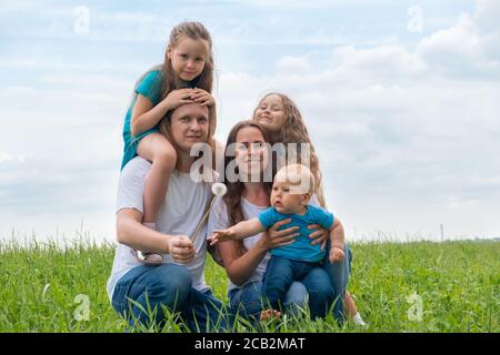 Ritratto grande famiglia papà, mamma e tre bambini su erba verde contro cielo blu. Felici genitori caucasici, due figlie e un figlio giovane Foto Stock