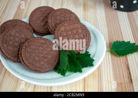 Porzioni di biscotti al cioccolato su sfondo di legno. Impilare i biscotti con scaglie di cioccolato. Biscotti al cioccolato sul piatto e una tazza nera in cerchi bianchi dopo Foto Stock