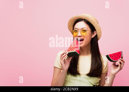 donna asiatica felice con bocca aperta che tiene affettato cocomero di carta isolato su rosa Foto Stock