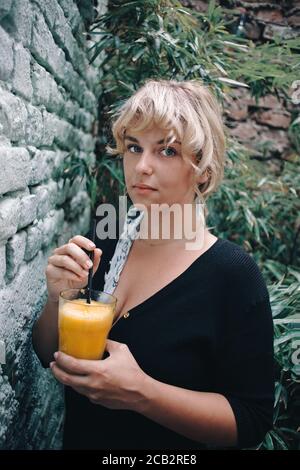 Bella giovane donna che beve succo d'arancia nel suo giardino Foto Stock