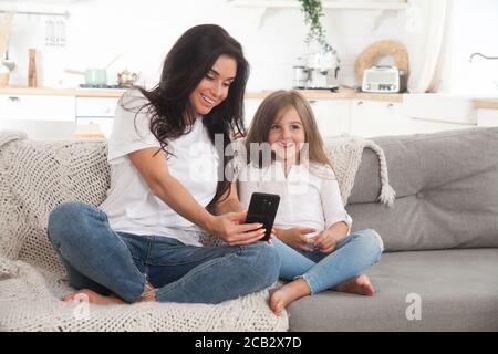 Giovane mamma e bambina che giocano online a casa utilizzando lo smartphone, chattando video o guardando film. Formazione a distanza. Video Foto Stock