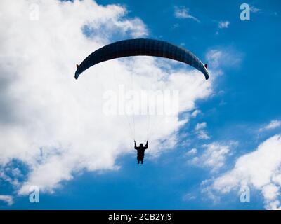 Silhouette di parapendio scuro sullo sfondo di cielo estivo blu e nuvole bianche. Tema sport adrenalinico. Foto Stock