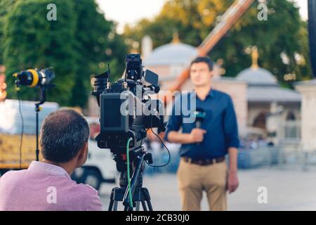 Concetto dietro la scena. Cameraman lavorando su fotocamera professionale che prende intervistatore TV, reporter di notizie professionale che fa le notizie all'aperto. Foto Stock