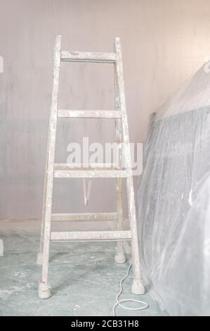 Scala in un locale vuoto coperto di fogli di polvere preparati per pittura e ristrutturazione Foto Stock