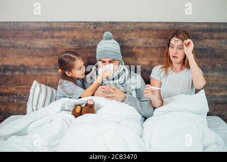 famiglia ammalata insieme a casa, moglie ammalata, marito e bambino sdraiati a letto insieme. trattamento, concetto di salute Foto Stock