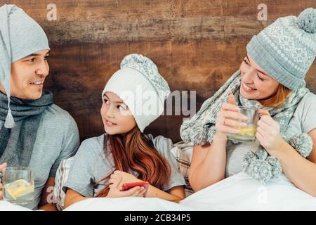 caucasica bella famiglia a letto che soffre di freddo, in grigio cappelli e sciarpe, malattia e concetto di malattia Foto Stock