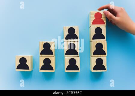 vista parziale della mano accanto a blocchi di legno con icone umane nere e rosse su sfondo blu, leadership e concetto di scala di carriera Foto Stock