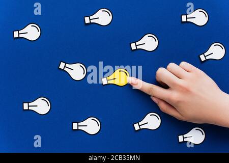 vista ritagliata della mano che punta alla lampadina della luce di carta su sfondo blu, concetto di business Foto Stock