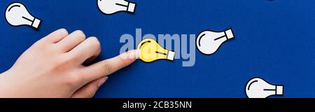 vista ritagliata della mano che punta alla lampadina della luce di carta su sfondo blu, concetto di business Foto Stock