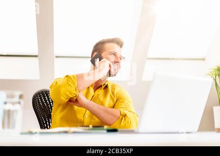 Foto di un uomo d'affari felice che fa una chiamata di lavoro mentre si siede dietro il suo laptop e lavora da casa. Ufficio domestico. Foto Stock