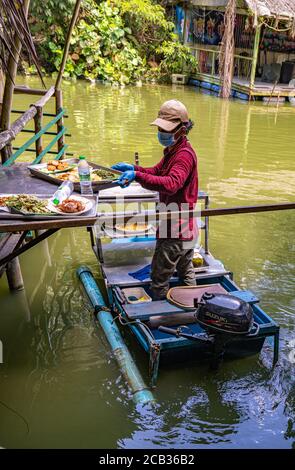 Il cameriere serve cibo da una barca tradizionale in un galleggiante Ristorante in stile tailandese Foto Stock