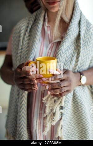 Vista a taglio di una coppia multietnica che si prende cura l'una dell'altra, l'uomo africano abbracciando dalla parte posteriore la sua donna europea, coperta di plaid lavorato a maglia e standin Foto Stock