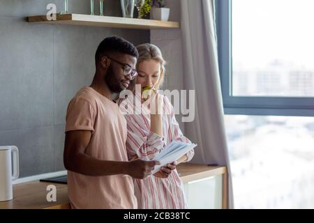 Giovane coppia multietnica stare in cucina, pianificare le loro vacanze estive congiunte, fare calcoli, sviluppare un percorso. Persone, vacanze, pianificazione Foto Stock