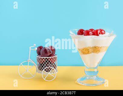 Un dessert di panna montata, gelato e biscotti e una piccola bicicletta con ciliegia maraschino in un bicchiere. Foto Stock