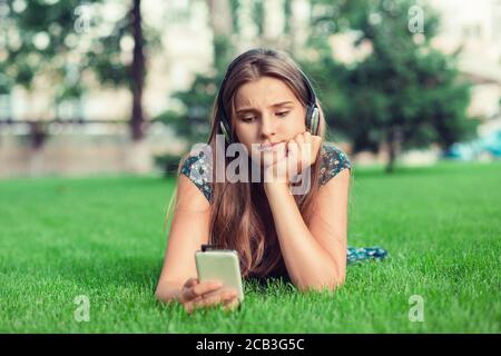 Closeup ritratto sconvolto triste scettica infelice grave donna che testava telefono dispiaciuto annoiò preoccupato con la conversazione sdraiata in città parco backgro Foto Stock