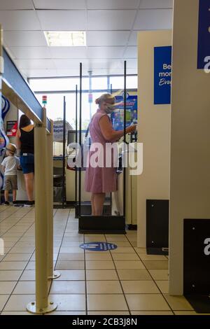 Una donna che indossa una maschera mentre si usa l'auto checkout in un supermercato Foto Stock