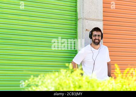 Un simpatico e trendy ragazzo della barba in cuffia che ascolta musica su sfondo colorato. Foto Stock