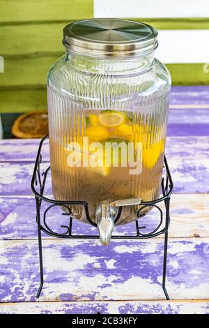 Limonata fatta in casa in vaso di vetro vintage con limoni e lime fette su un tavolo di legno, verticale Foto Stock