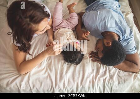 Felice giovane padre, madre e simpatico bambino ragazzo sdraiato sul letto, vista dall'alto foto. Tempo libero e libero Foto Stock