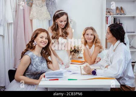 donna sarto designer creare un nuovo elegante abito da sposa alla moda insieme con belle giovani modelli caucasici ragazze, attentamente ascoltare lui Foto Stock