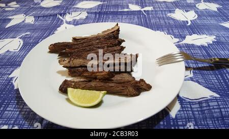 Barbecue Picanha al limone, servito su un piatto bianco con forchetta, su una tovaglia blu con motivi floreali, Brasile, Sud America Foto Stock