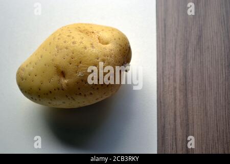 Patata. Patata, tubero con nome scientifico solanum tuberosum, su sfondo bianco e legno, con foto ingrandita con spazio copia. Foto Stock