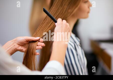 acconciatore acconciato irriconoscibile che lavora con i capelli del cliente, pettinatura e taglio dei capelli lunghi in salone di bellezza. Bellezza, concetto di moda Foto Stock