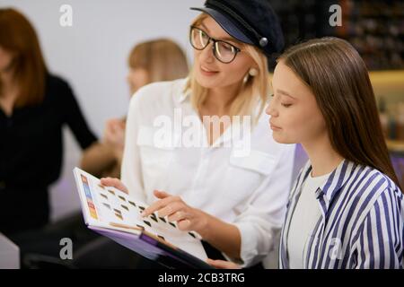 parrucchiere moderno ed elegante che dà consiglio al cliente quale colore scegliere, quale colore è adatto per la tintura, tenendo la tavolozza dei colori e l'aspetto Foto Stock