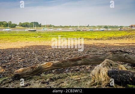 Tronco d'albero su mudflats a bassa marea con barche a vela in distanza Foto Stock