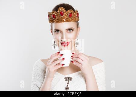 Gustando la sua tazza di tè del caffè. Sorridente bellezza regina principessa sposa di essere bella donna, tazza bianca di bevanda calda in mano isolato su bianco grigio ba Foto Stock