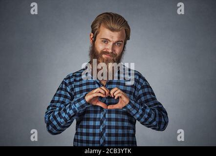 Ritratto di felice bell'uomo bearded che fa il gesto del cuore con le dita. Hipster maschio con barba in camicetta a scacchi in plaid blu isolato su grigio Foto Stock