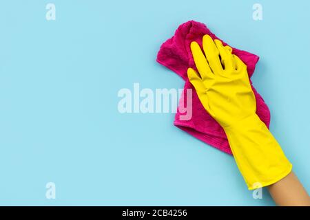 Mano della donna in guanto giallo di gomma da sfondo blu straccio. Foto Stock