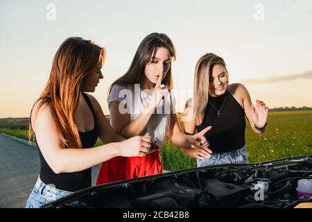 Tre amiche hanno avuto problemi durante il viaggio fuori città, aprire il cofano per controllare i dettagli e cercare di calmarsi Foto Stock