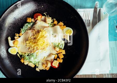 Crostini, pomodori, uova, formaggio e insalata di erbe in un piatto scuro accanto alle posate Foto Stock