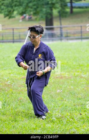 Un uomo cinese americano che indossa uno scudo per il viso frequenta una lezione di Tai Chi al Kissena Park a Flushing, New York City. Foto Stock