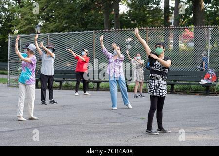 Donne di varie età ed etnie frequentano una lezione di Tai Chi al mattino che indossa maschere chirurgiche e divaricazioni sociali. In Queens, New York City. Foto Stock