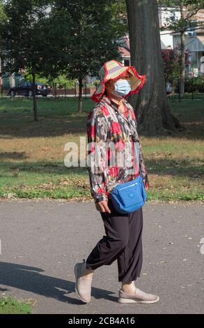 Una donna cinese americana che indossa una maschera chirurgica e abiti colorati, passeggiate in esercizio nel Kissena Park a Flushing, New York. Foto Stock