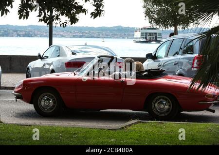 Coppia in cabriolet rosso d'annata Alfa Romeo Giulietta Spider a Sirmione, Lago di Garda, Italia Foto Stock